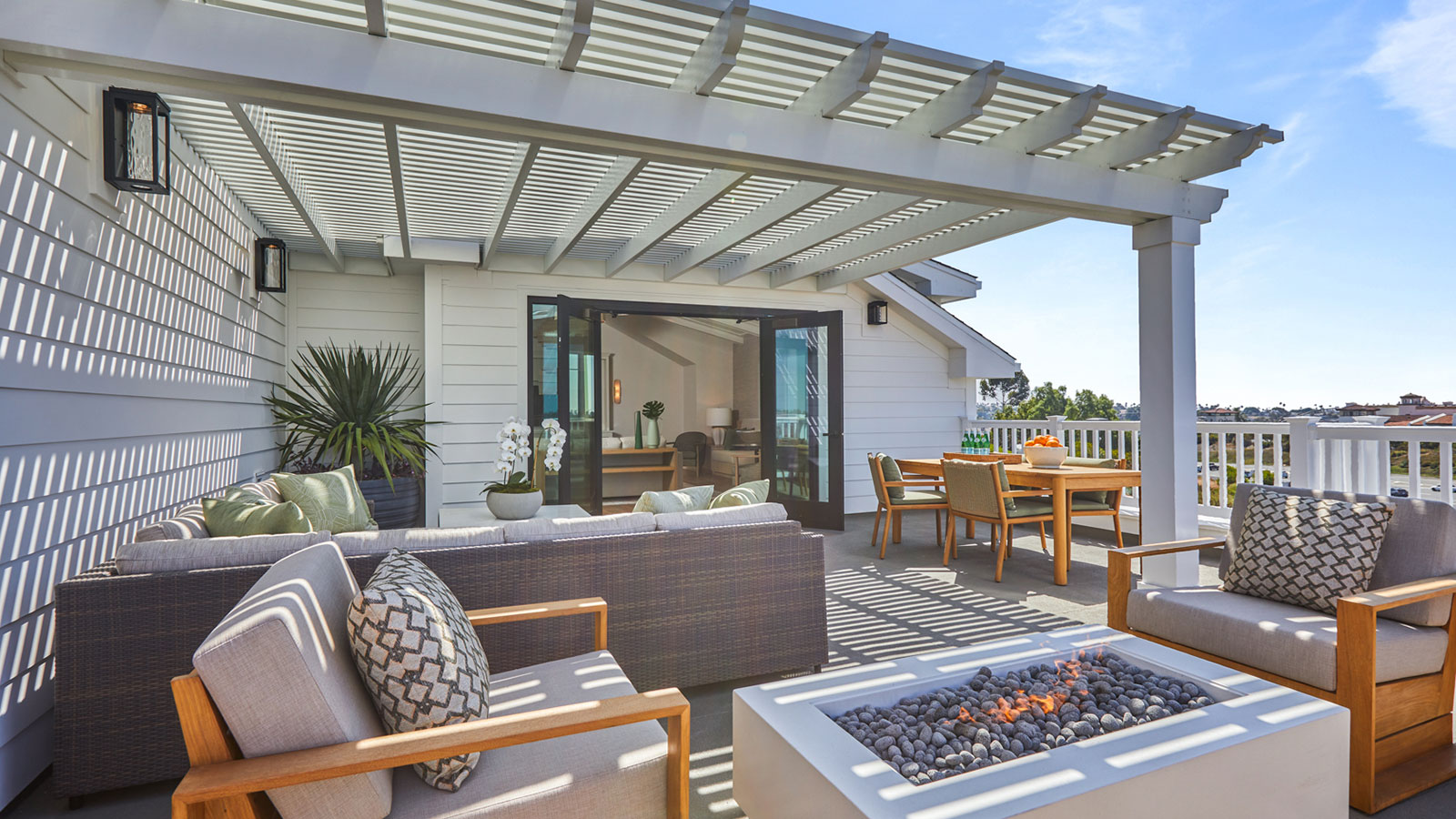 This is a photo of The Seville's community room terrace, which features a fire pit, outdoor seating and a white pergola.