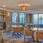 This is a photo of The Seville's assisted living dining room. The room is filled with chairs, features a fireplace, and has floor-to-ceiling windows.