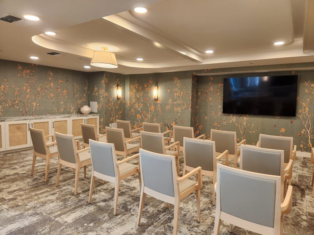 Upscale senior living room with a row of chairs and television with calming colors at The Seville